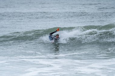 Bulutlu bir kış gününde, sörf yaparak okyanusta 360 numara yapan sörfçü..