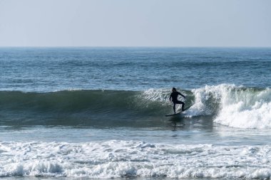 Portekiz, Furadouro sahilinde sörf yapan bir sörfçü. Okyanusta dalgaları yakalayan adamlar. Su sörfü sporu. Su sporları dersleri ve plaj yüzme aktiviteleri.
