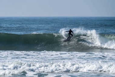 Portekiz, Furadouro sahilinde sörf yapan bir sörfçü. Okyanusta dalgaları yakalayan adamlar. Su sörfü sporu. Su sporları dersleri ve plaj yüzme aktiviteleri.