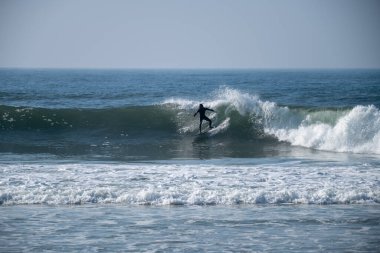 Portekiz, Furadouro sahilinde sörf yapan bir sörfçü. Okyanusta dalgaları yakalayan adamlar. Su sörfü sporu. Su sporları dersleri ve plaj yüzme aktiviteleri.