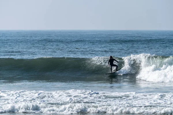 Portekiz, Furadouro sahilinde sörf yapan bir sörfçü. Okyanusta dalgaları yakalayan adamlar. Su sörfü sporu. Su sporları dersleri ve plaj yüzme aktiviteleri.