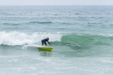 Portekiz, Furadouro plajında sörf tahtası ile sörf yapan bir sörfçü. Okyanusta dalgaları yakalayan adamlar. Su sörfü sporu.