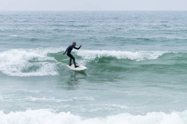 Portekiz, Furadouro plajında sörf tahtası ile sörf yapan bir sörfçü. Okyanusta dalgaları yakalayan adamlar. Su sörfü sporu.