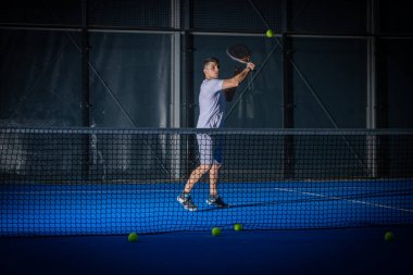 Beyaz tişörtlü sportif Avrupalı adam kapalı alanda Padel tenis oynuyor