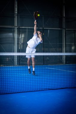Beyaz tişörtlü sportif Avrupalı adam kapalı alanda Padel tenis oynuyor