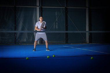 Beyaz tişörtlü sportif Avrupalı adam kapalı alanda Padel tenis oynuyor