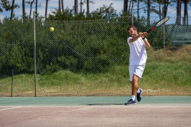 Tenis oyuncusu sahada raketle forehand vuruyor..