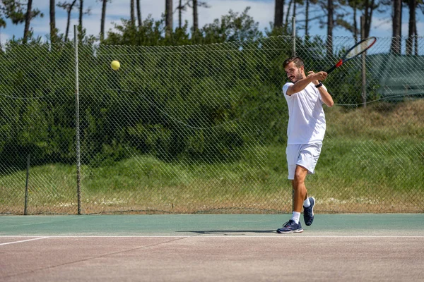 Tennis player hitting forehand at ball with racket on court.