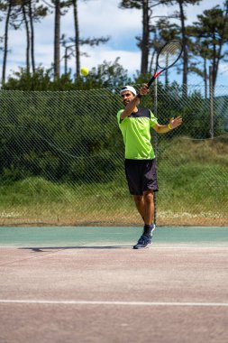 Tenis oyuncusu sahada raketle forehand vuruyor..
