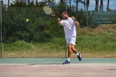 Tenis oyuncusu sahada raketle forehand vuruyor..