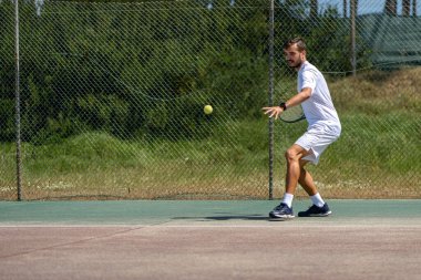 Tenis oyuncusu sahada raketle forehand vuruyor..