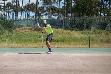 Tenis oyuncusu sahada raketle forehand vuruyor..