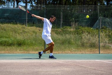 Tenisçi sahada raketle ters vuruş yapıyor..