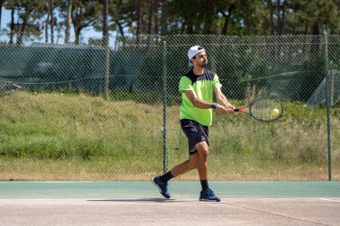 Tenisçi sahada raketle ters vuruş yapıyor..