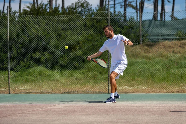 Tennis player hitting forehand at ball with racket on court.