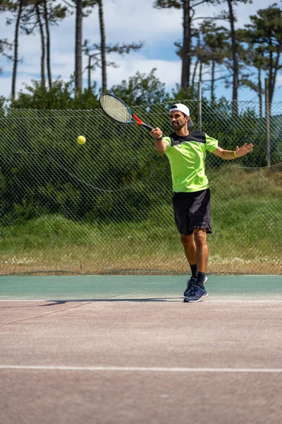 Tennis player hitting forehand at ball with racket on court.