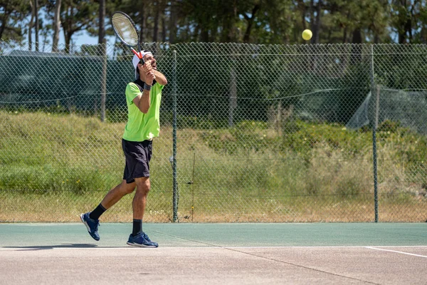 Tennis player hitting backhand at ball with racket on court.