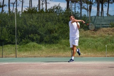 Tenis oyuncusu sahada raketle forehand vuruyor..
