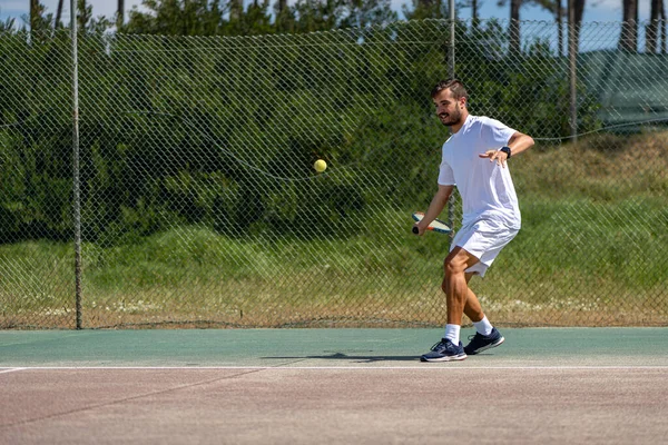 Tennis player hitting forehand at ball with racket on court.