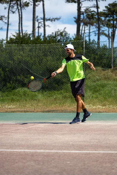 Tennis player hitting forehand at ball with racket on court.