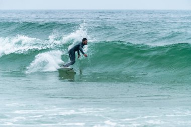 Sörfçü sisli bir sabahta sörf yapıyor Furadouro sahilinde, Ovar - Portekiz.