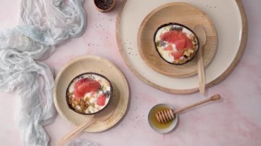 Yogurt with grapefruit, granola, chia and honey served in half a coconut shell on a rose marble kitchen countertop.