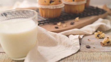 Chocolate chip muffins with milk served on glass cups on white kitchen countertop.