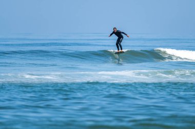 Parlak güneşli bir günde denizde sörf yapan orta yaşlı bir adam.