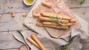 Traditional italian breadsticks grissini with rosemary, olive oil and sesame seeds on wooden countertop.