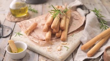 Traditional italian breadsticks grissini with rosemary, olive oil and sesame seeds on wooden countertop.