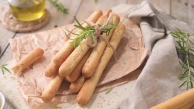 Traditional italian breadsticks grissini with rosemary, olive oil and sesame seeds on wooden countertop.