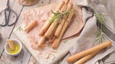 Traditional italian breadsticks grissini with rosemary, olive oil and sesame seeds on wooden countertop.