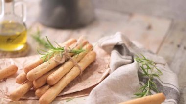 Traditional italian breadsticks grissini with rosemary, olive oil and sesame seeds on wooden countertop.