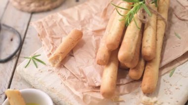 Traditional italian breadsticks grissini with rosemary, olive oil and sesame seeds on wooden countertop.