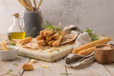 Traditional italian breadsticks grissini with rosemary, olive oil and sesame seeds on wooden countertop.