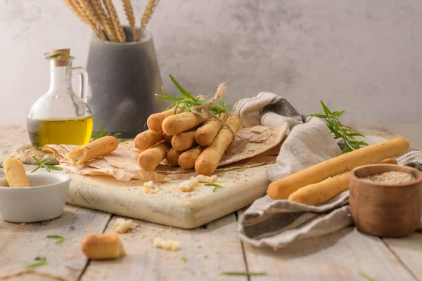 Traditional italian breadsticks grissini with rosemary, olive oil and sesame seeds on wooden countertop.