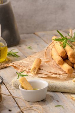 Traditional italian breadsticks grissini with rosemary, olive oil and sesame seeds on wooden countertop.