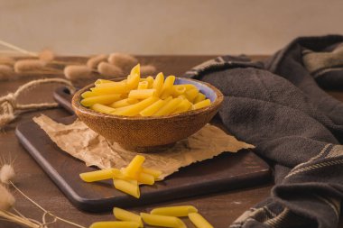 Penne pasta in wooden cutting board on rustic kitchen countertop.