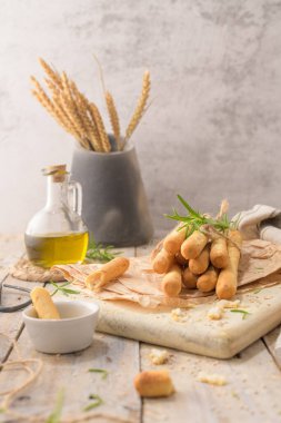 Traditional italian breadsticks grissini with rosemary, olive oil and sesame seeds on wooden countertop.