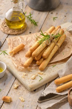 Traditional italian breadsticks grissini with rosemary, olive oil and sesame seeds on wooden countertop.