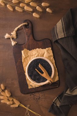 Black sesame seeds in a ceramic bowl on a rustic kitchen countertop.