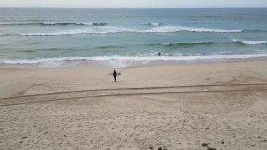 Dalgıç kıyafeti giyen sörfçüler bulutlu bir öğleden sonra deniz kenarında sörf tahtası tutuyorlar..