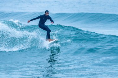 Sörfçü sisli bir sabahta sörf yapıyor Furadouro sahilinde, Ovar - Portekiz.