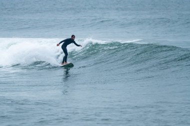 Sörfçü sisli bir sabahta sörf yapıyor Furadouro sahilinde, Ovar - Portekiz.