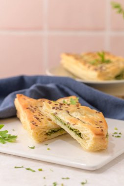 Ispanaklı puf böreği, ricotta peyniri ve maydanoz yapraklarıyla mutfak tezgahındaki beyaz seramik tabaklarda..