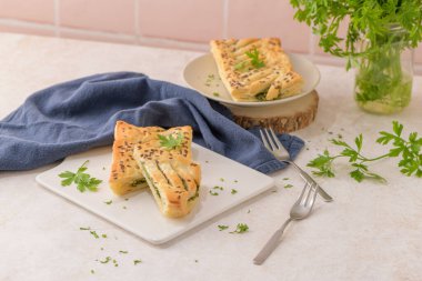 Ispanaklı puf böreği, ricotta peyniri ve maydanoz yapraklarıyla mutfak tezgahındaki beyaz seramik tabaklarda..