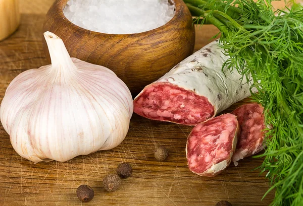 Rebanadas de salame en la tabla de cortar, con eneldo, pimienta, sal — Foto de Stock