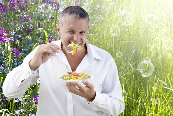 Dorosły człowiek jedzenie sałatką ze świeżych warzyw na tle lato natura — Zdjęcie stockowe