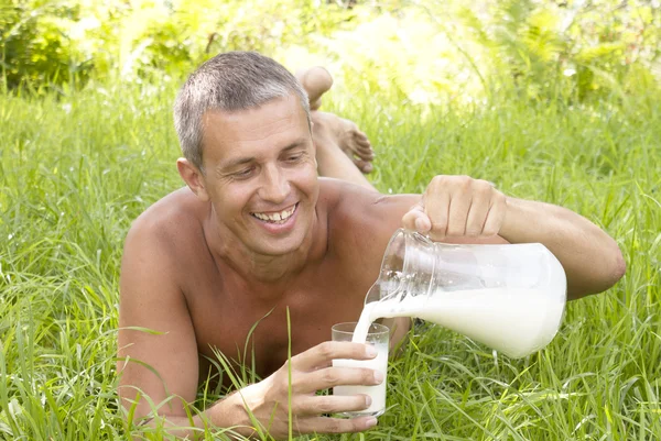 De gelukkig volwassen man drinkt verse melk bij groen gras — Stockfoto