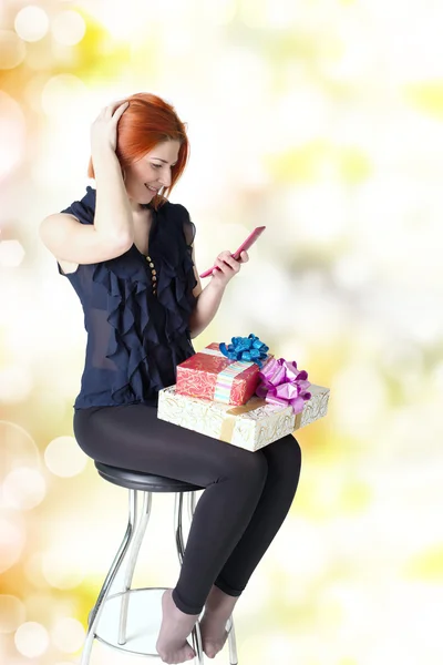 Chica feliz en una silla con un teléfono y una caja de regalo —  Fotos de Stock